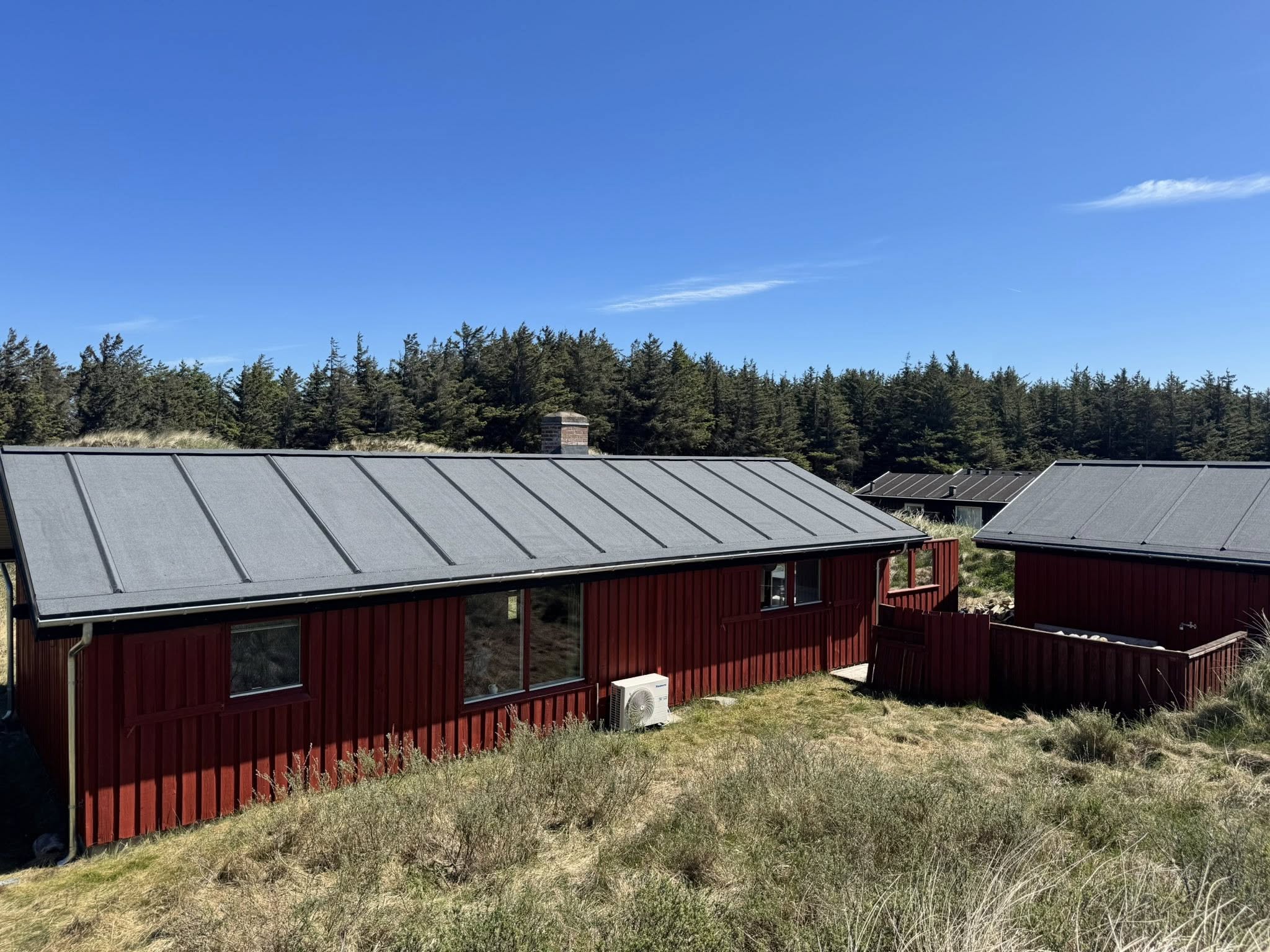 Rødt sommerhus i klitlandskab med nyt mørkt tag